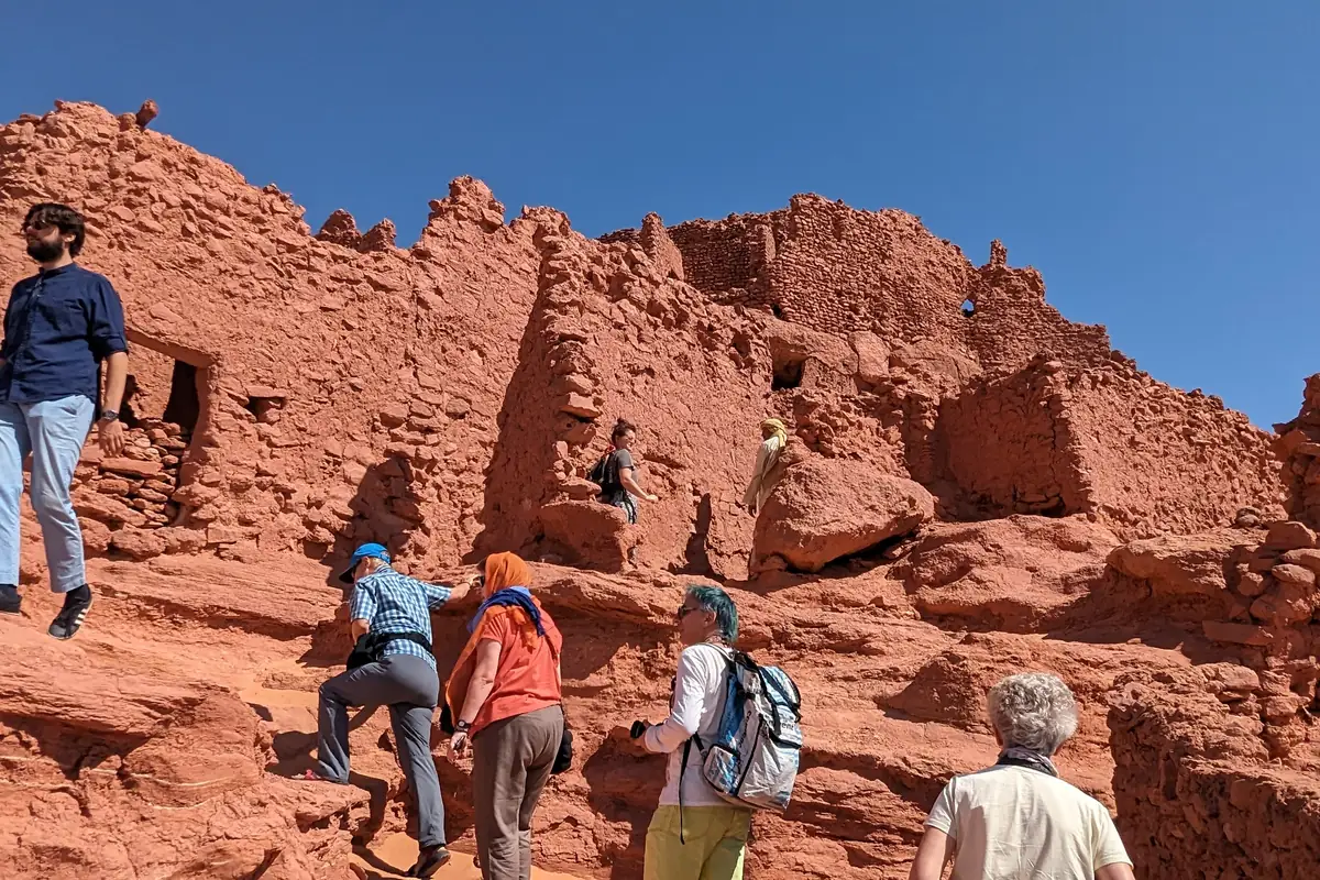 Des voyageurs gravissant les murs de terre rouge du vieux ksar de Timimoun