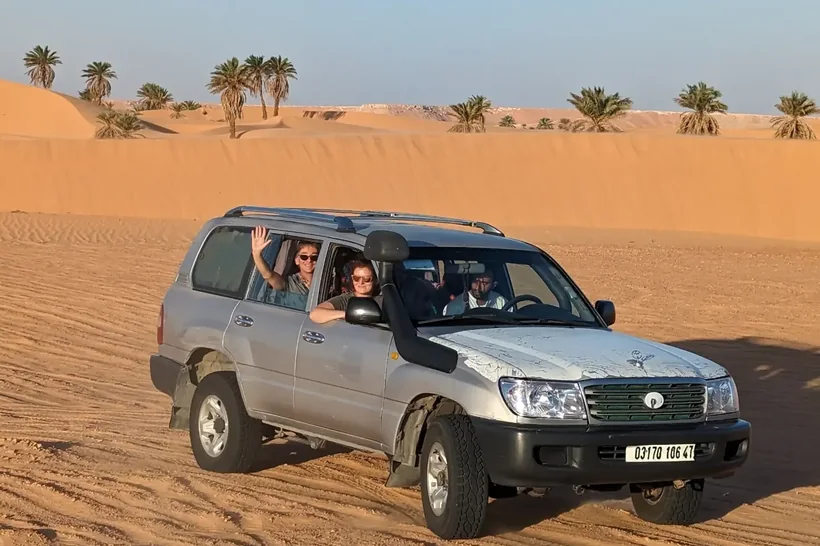 Des voyageurs saluant depuis un 4x4 traversant les dunes près d’El Menia