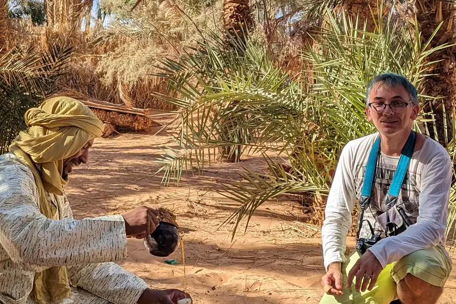 Un hôte préparant le thé pour une voyageuse dans une palmeraie de Timimoun